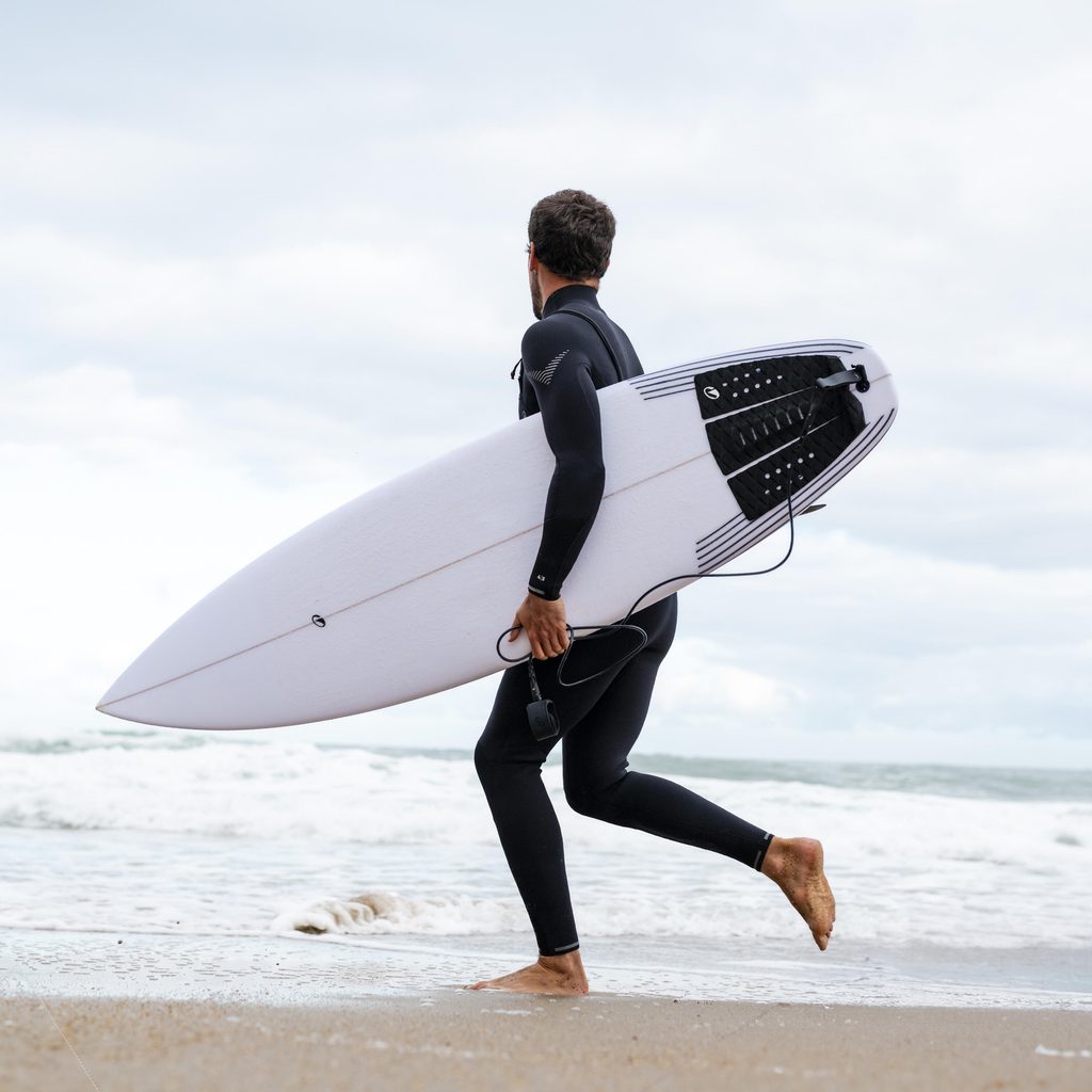 Surfeur regardant le line up en combinaison Decathlon 4/3 900 avec sa planche de surf sous le bras