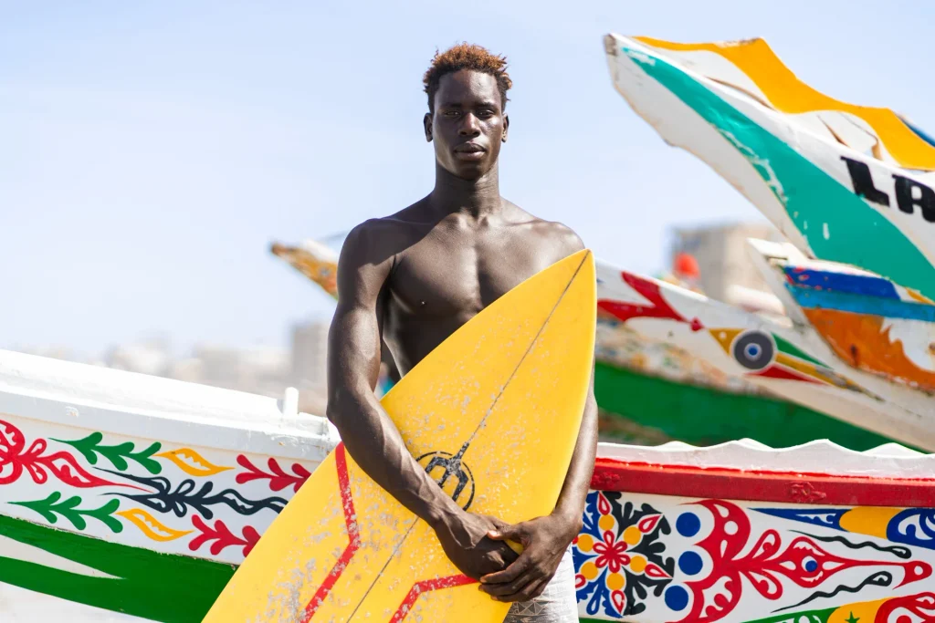 Fallou Bousso sur le spot de Ouakam à Dakar, avec des barques colorées de pécheurs typiques du Sénégal.